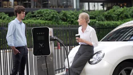 progressive businessman and businesswoman leaning on ev car and charging point.