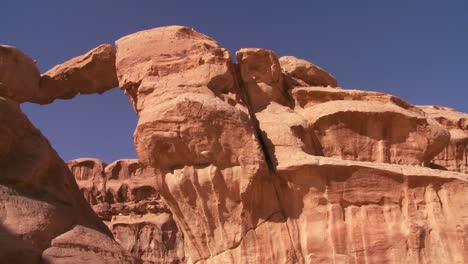 pan across to an amazing arch formation in the sadi desert in wadi rum jordan with a bedouin man walking through