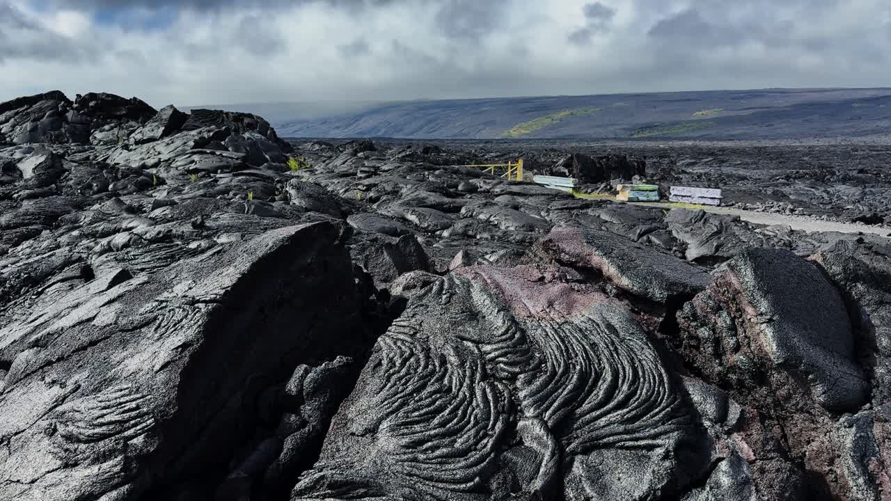 Gambar statis aliran lava padat hitam dengan tekstur vulkanik di bawah langit berawan