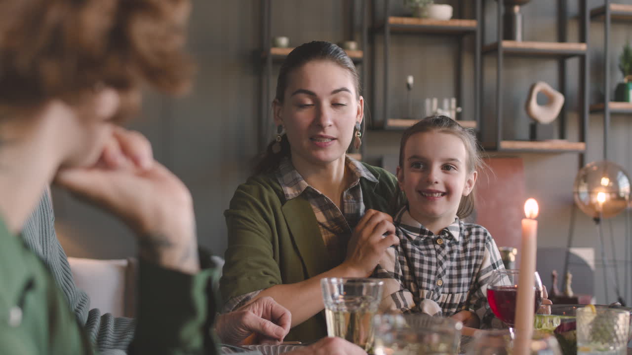 Madre seduta a tavola con la sua adorabile bambina che parla con la sua famiglia mentre consumano un pasto insieme.