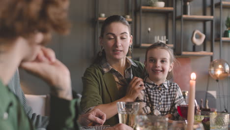 mother sitting at dinner table with her cute little girl and talking to her family while having a meal together