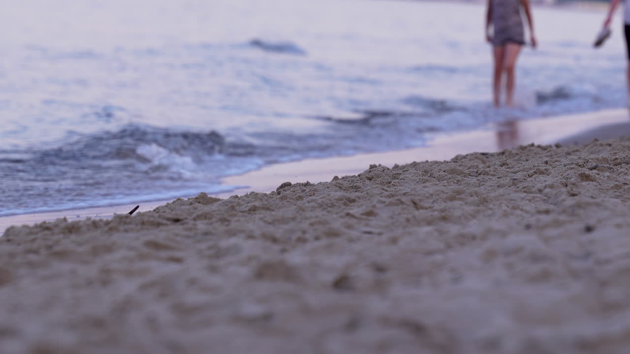 Person walking on sandy beach, blurred in background with calm sea waves