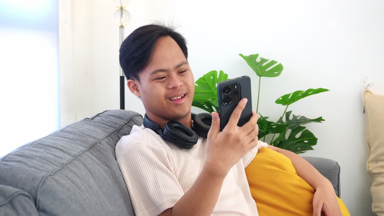 Joyful young asian man with asperger video chatting on phone while spreading smiles at home