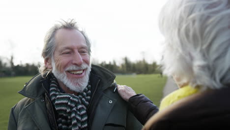 woman ties mans scarf as senior couple enjoying autumn or winter walk through park together