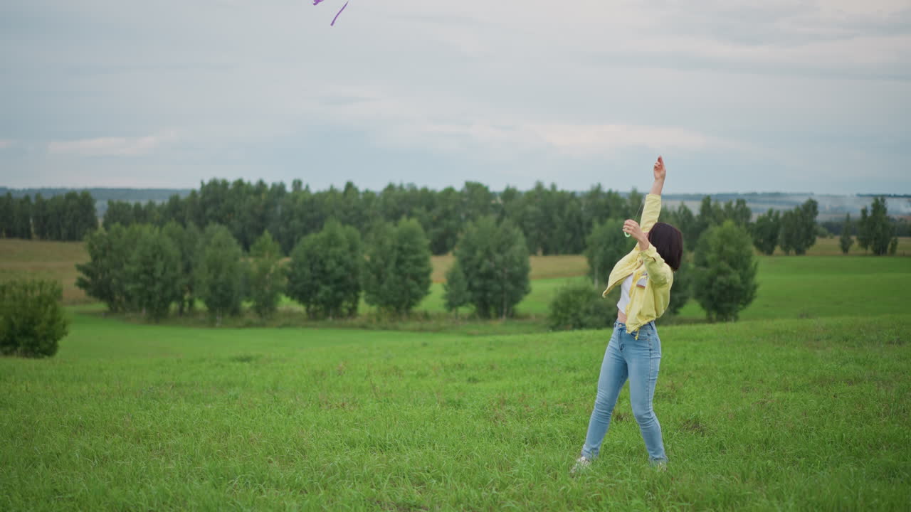 Mujer soltando una cometa arcoíris al cielo, un extenso campo verde, línea de árboles distante, viento constante que levanta la colorida vela, postura enérgica con el brazo levantado, colas juguetonas ondeando, escena inspiradora al aire libre
