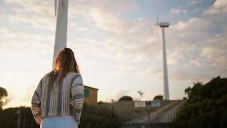 Zeitlupenaufnahme-Einer-Frau,-Die-Auf-Windmühlen-Zugeht,-Die-Sich-Bei-Sonnenuntergang-Drehen