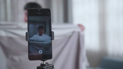 display smartphone of asian boy shows trick with disappearing on mobile phone camera while recording video content for social networks in cozy room