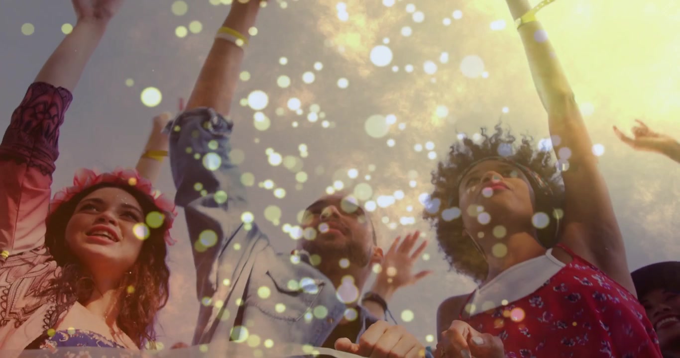 Tre adulti che alzano le braccia, esultando mentre inizia la musica del festival, con coriandoli bokeh che fluttuano sui volti.