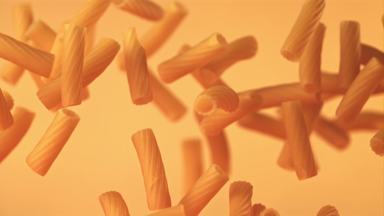 Pasta rigatoni cruda che cade al rallentatore su uno sfondo arancione