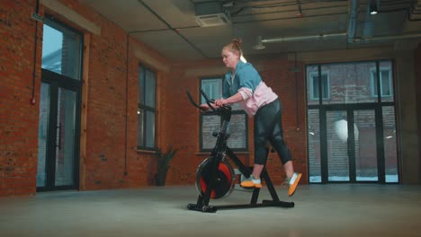 Chica-Atlética-Realizando-Ejercicios-De-Entrenamiento-Aeróbico-En-Bicicleta-Estacionaria-En-Un-Gimnasio-Con-Niebla