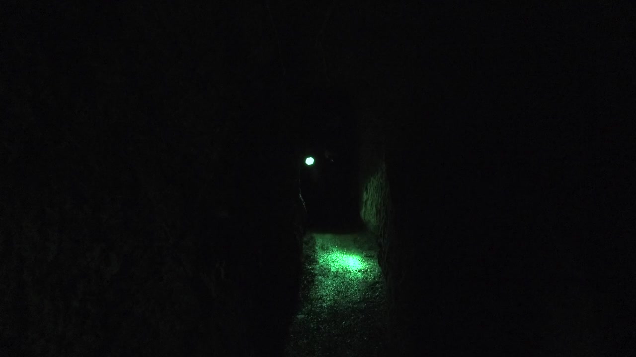 Person Walking Through Dark Cave With Green Flashlight