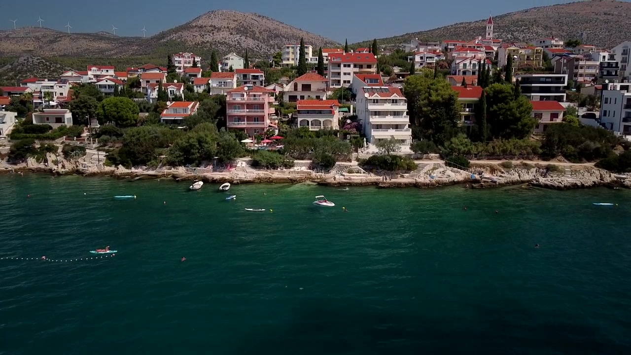 Seget Vranjica, Trogir, Hırvatistan'da kırmızı çatılı evlerin berrak Adriyatik kıyısında sıralandığı, havadan orta seviye iniş yaklaşımı