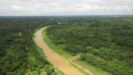 wide rotating drone shot with a boat coming down the amazon river and the rainforest surrounding the river in peru