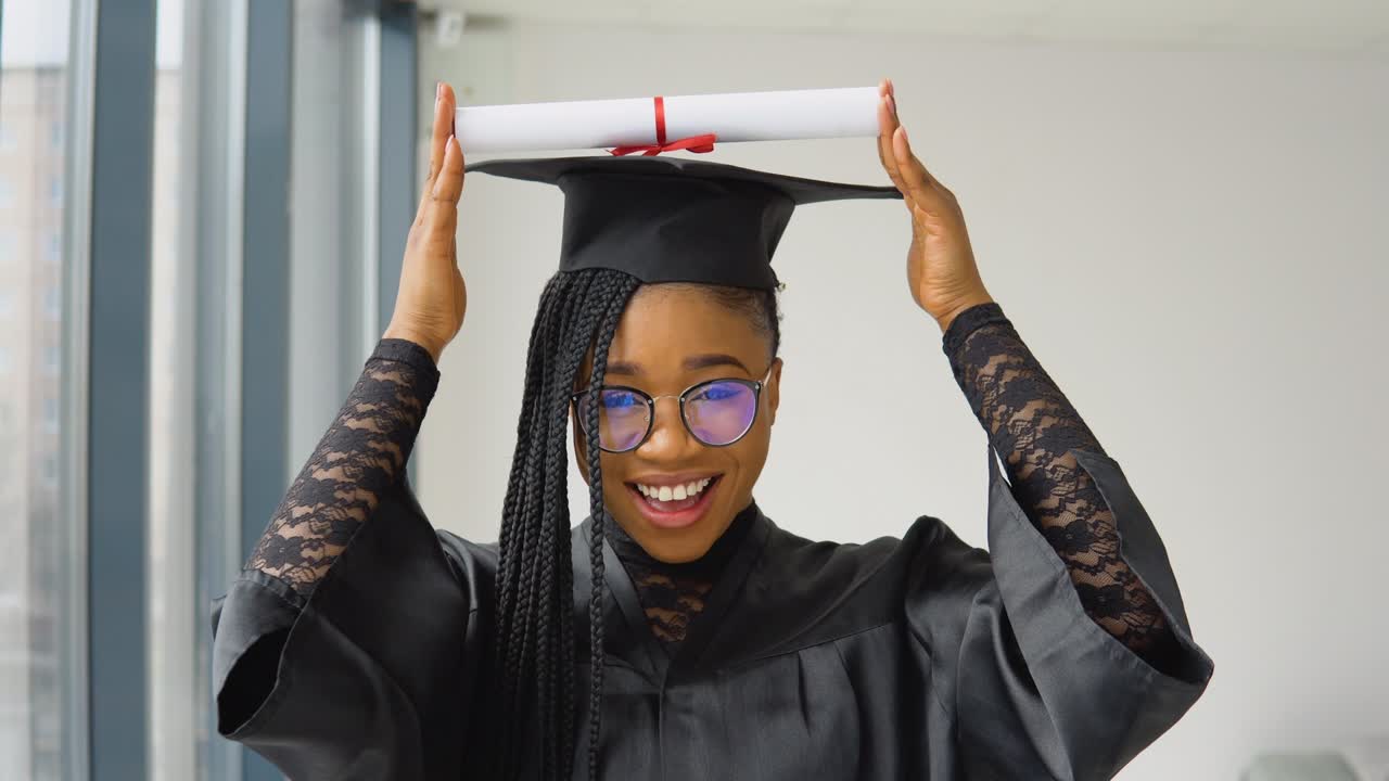 una alegre graduada africana sostiene un diploma sobre su cabeza y posa para la cámara en la universidad. la educación superior está disponible para las mujeres