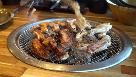 korean barbecue built in grill in table turning pieces of chicken in restaurant