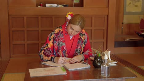 Young-latin-woman-practicing-japanese-writing-at-Okinawa-world-wearing-kimono-Ryusou-dress-in-traditional-japan-wood-house-durgin-summer
