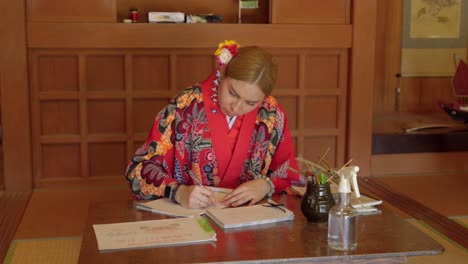 young latin woman practicing japanese writing at okinawa world wearing kimono ryusou dress in traditional japan wood house durgin summer