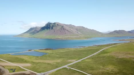 A-straight-flight-path-shot-of-a-large-vibrant-green-mountain-surrounded-by-a-lake-in-Iceland