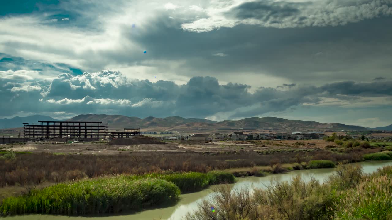 Huge cumulus clouds billowing over the town, mountains, and river - tilt down, sliding motion time lapse