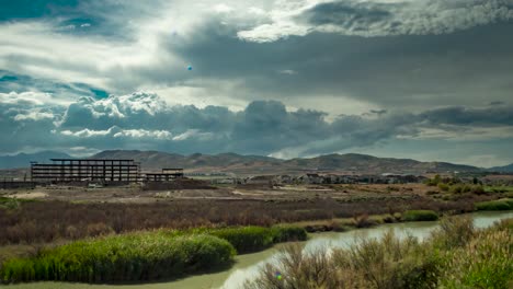 Huge-cumulus-clouds-billowing-over-the-town,-mountains,-and-river---tilt-down,-sliding-motion-time-lapse