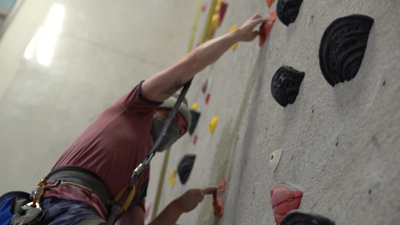 Rock climber climbing an indoor rock wall using athletic chalk for grip.