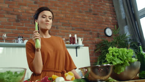 mujer degustando apio fresco en la cocina. bruneta alegre cocinando comida saludable.