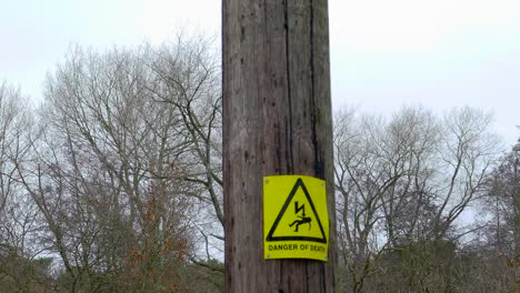 tiro inclinado que revela una señal de advertencia de color amarillo brillante montada en un poste de goma de madera, la señal que indica el peligro potencial y la posibilidad de muerte por el voltaje y la corriente transportados arriba en norfolk