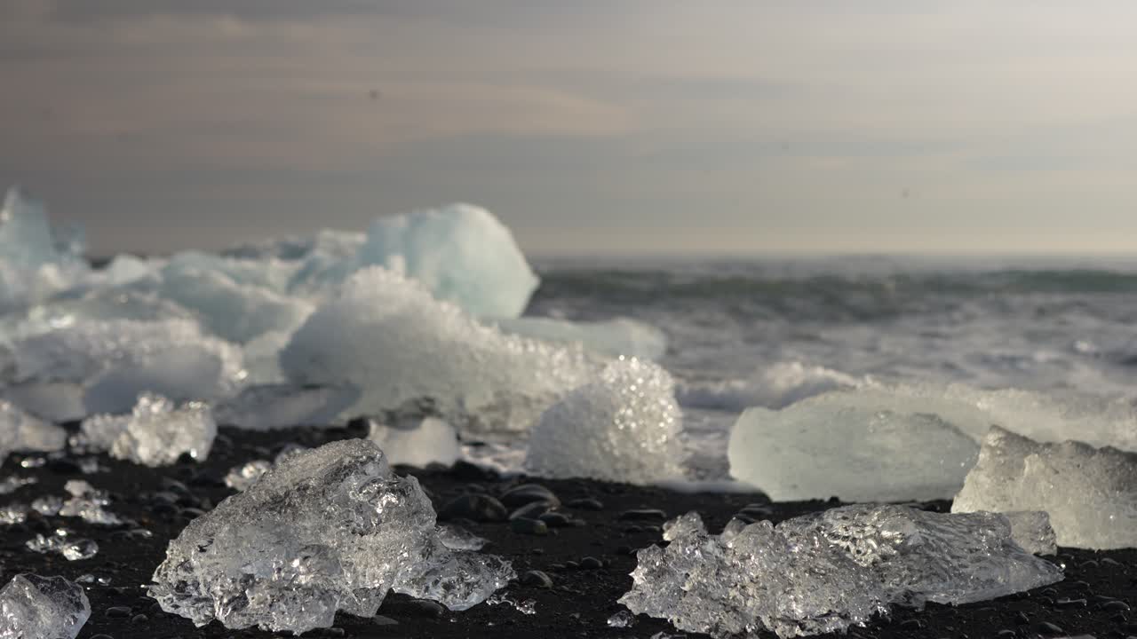 Beautiful glacier ice pieces shining on black sand beach with ocean waves in Iceland, stunning frozen landscapes