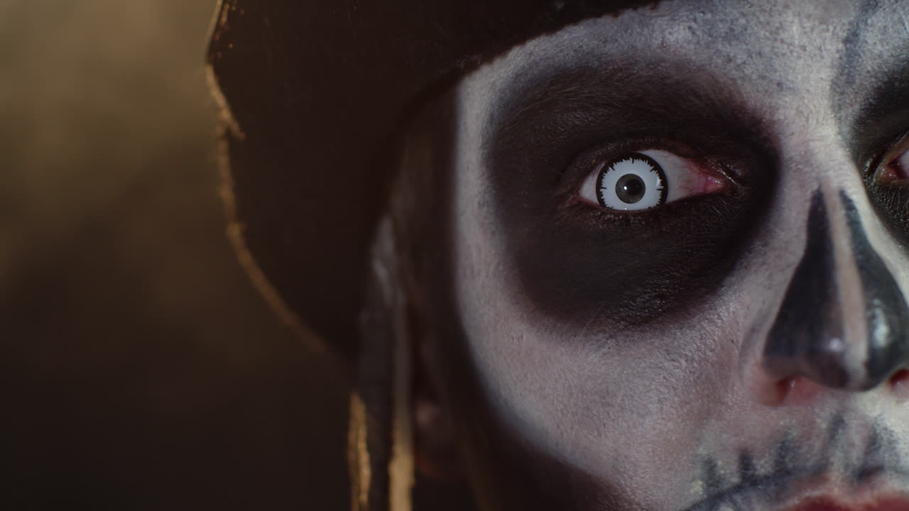 Close-up shot of face in skeleton Halloween makeup opening eyes with white pupil, trying to scare
