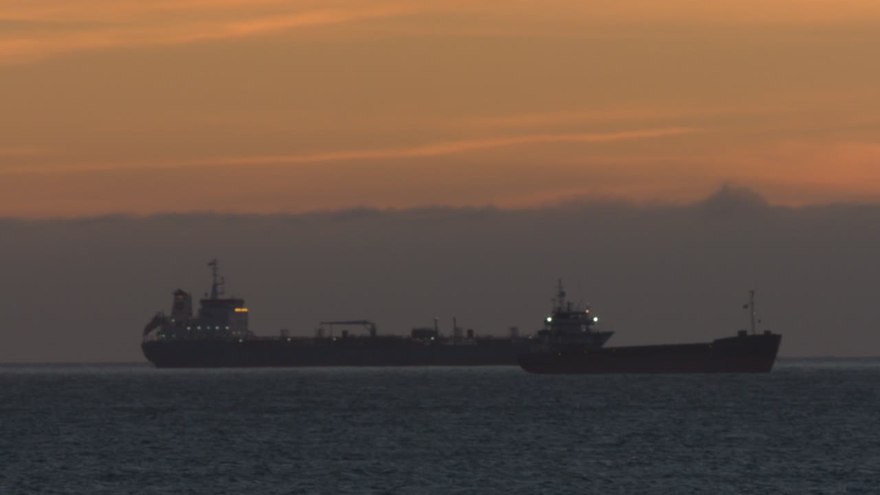 범선은 주황색 일몰 동안 물 위를 활공합니다.