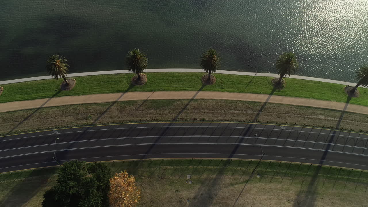 Smooth aerial perspective tracking runner and traffic moving along Albert Park Lake, Melbourne, Australia.