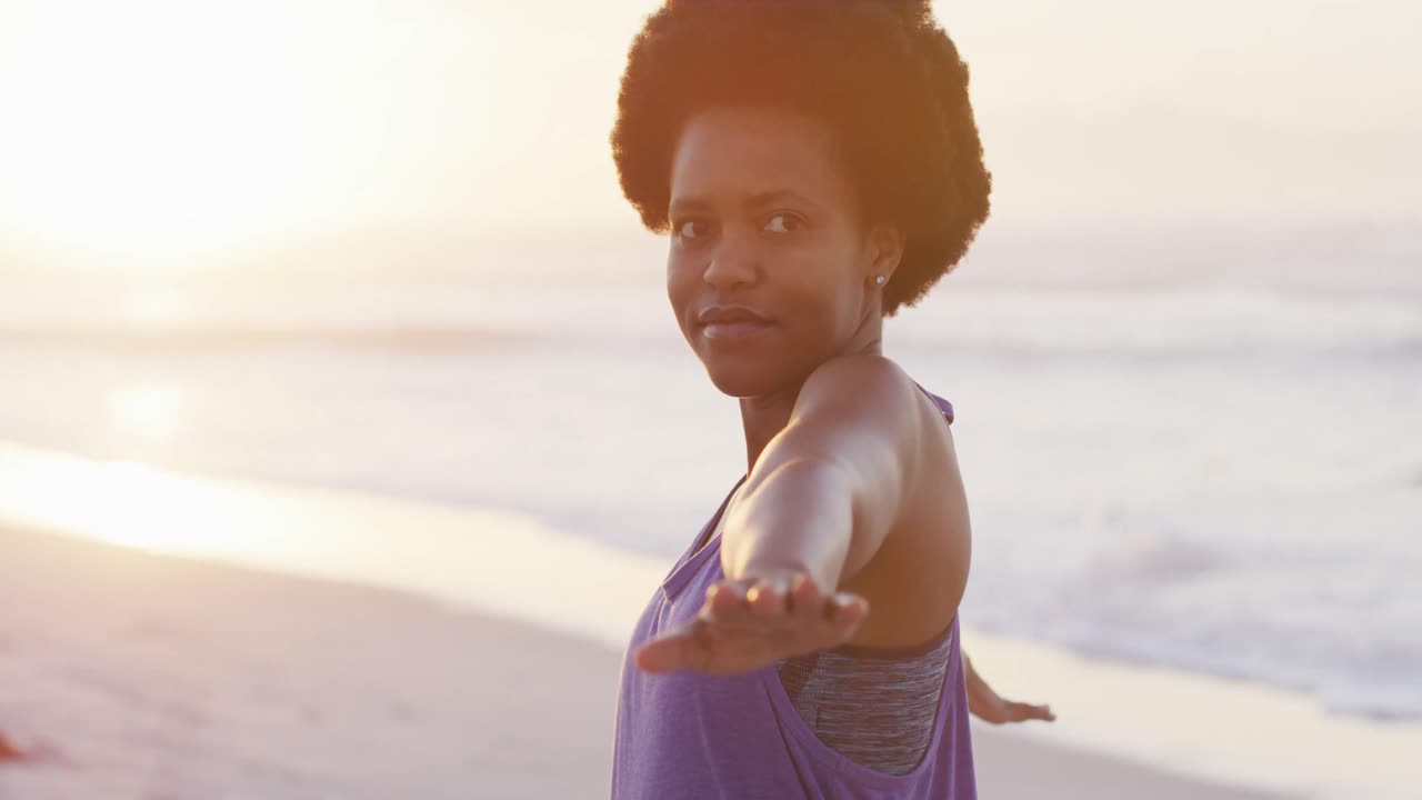 Donna afroamericana felice che pratica yoga su una spiaggia soleggiata.