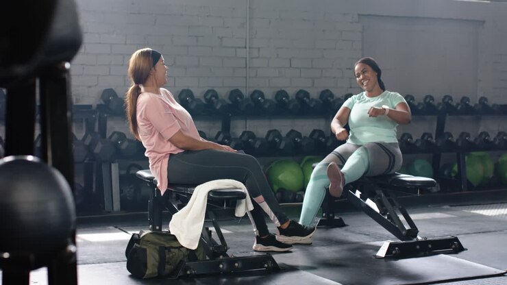 Diverse female pals in gym mint woman raising hand sparking high fives laughing checking smartwatch