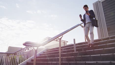 Asian-man-holding-coffee-cup-using-smartphone-running-down-the-stairs-at-corporate-park