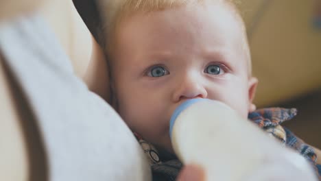 mother feeds little baby with tasty milk mix in light room