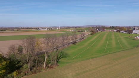 an aerial view of a single rail road track going thru country farmlands as a steam train approaches in the distance on a sunny fall day