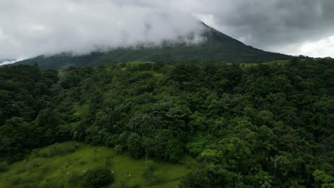 aerial view moving forward shot, approaching the arena volcano in costa rica, clouds covering the volcano in the background