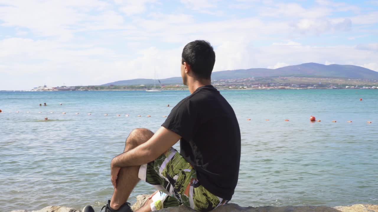 해변에 앉아 바다와 산의 전망을 즐기는 남자