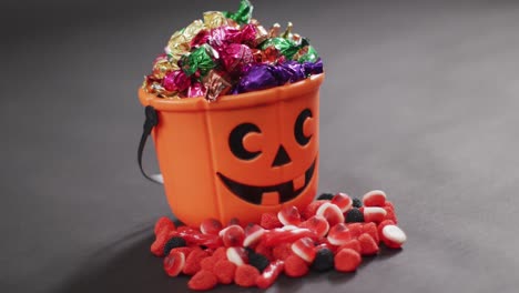 Scary-halloween-pumpkin-printed-bucket-full-of-candies-against-grey-background