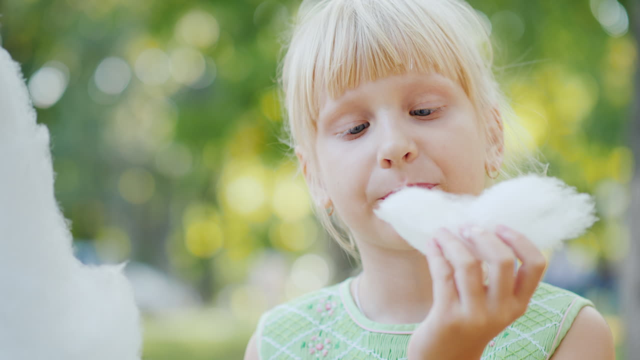 La bambina sta mangiando del delizioso zucchero filato al parco e si lecca le dita. Video 4k.