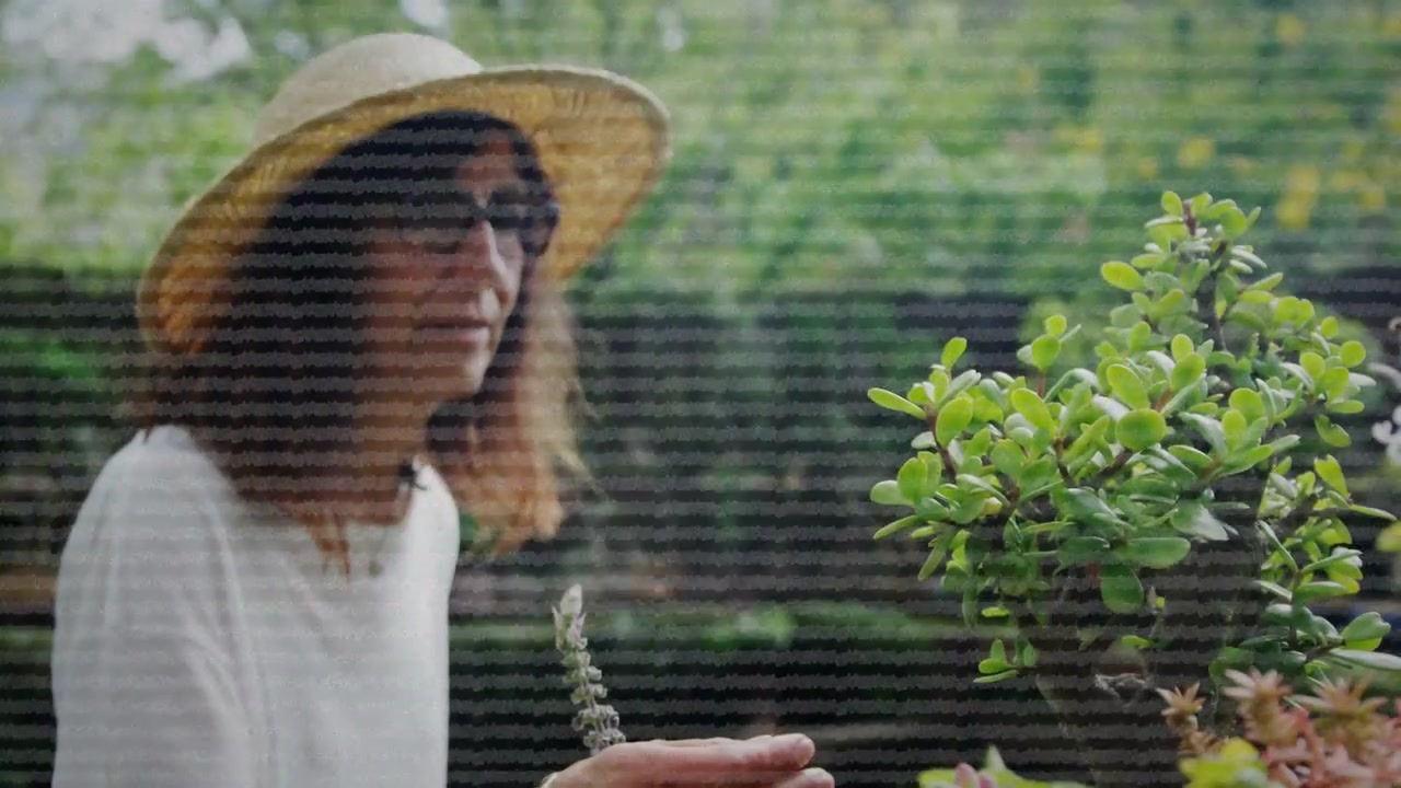 Woman walking into garden, pausing and inspecting bloom and tending pots, UI overlays obscuring her