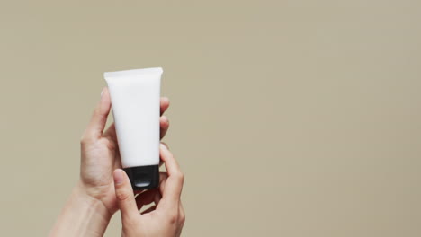 hands of woman with tube of cream on beige background with copy space, slow motion