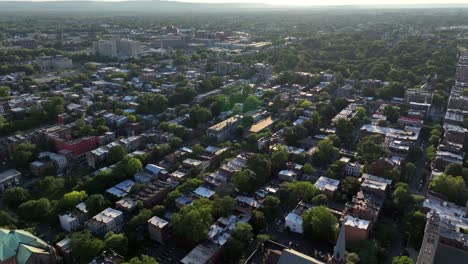quiet idyllic housing area in suburb of town. sunset time in summer. green trees on roads. downtown blocks of albany, new york in background. aerial wide shot. serene atmosphere