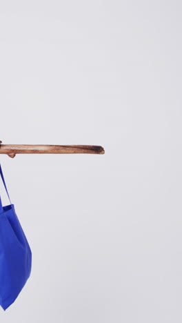 vertical video of blue and white canvas bag hanging from branch with copy space on white background
