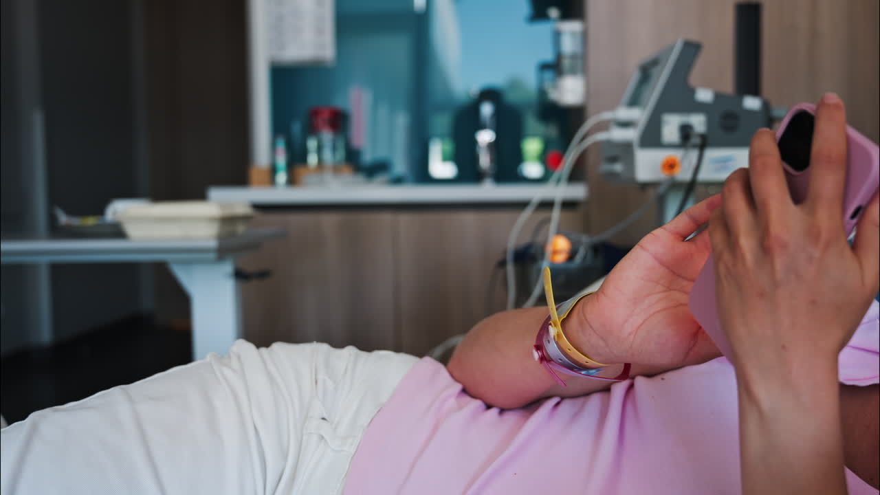 Pregnant woman scrolling on her phone while lying in a hospital bed at the doctor's office