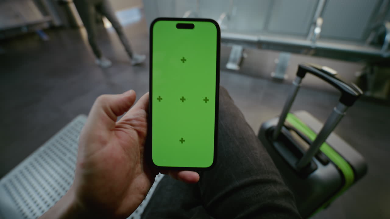 Person holding a smartphone with a green screen in a train station