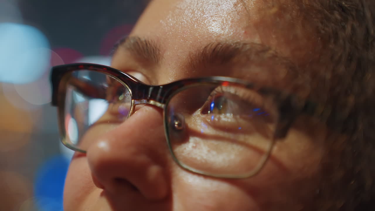 Primo piano di occhi e occhiali che riflettono le luci della città, ritratto notturno contemplativo con bokeh scintillante, sguardo verso l'alto pieno di meraviglia e introspezione, riflessi caldi sulle lenti, incarnato delicato