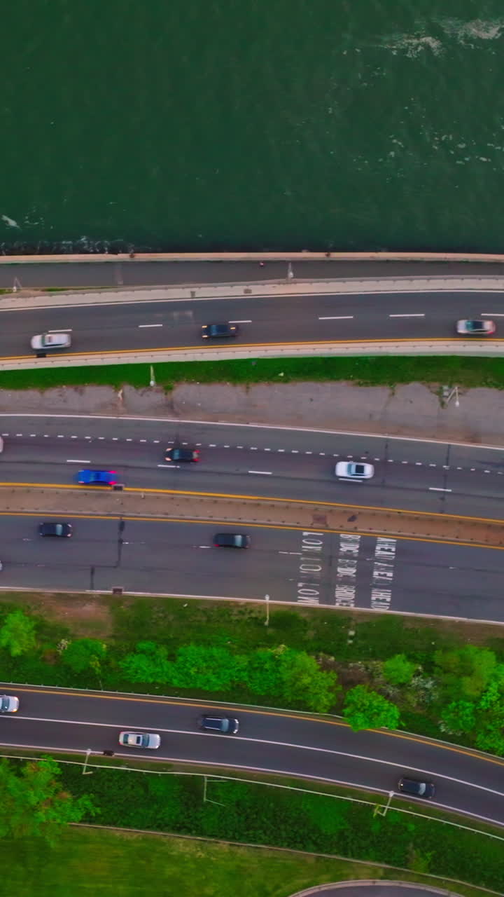Few roads going through the green bank of the river. Aerial perspective on the motorways and cars going on. Vertical video