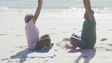 una feliz pareja afroamericana haciendo yoga y meditando en la playa, en cámara lenta