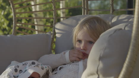 Portrait-of-a-cute-blonde-toddler-girl-thinking-as-she-swings-on-a-swing